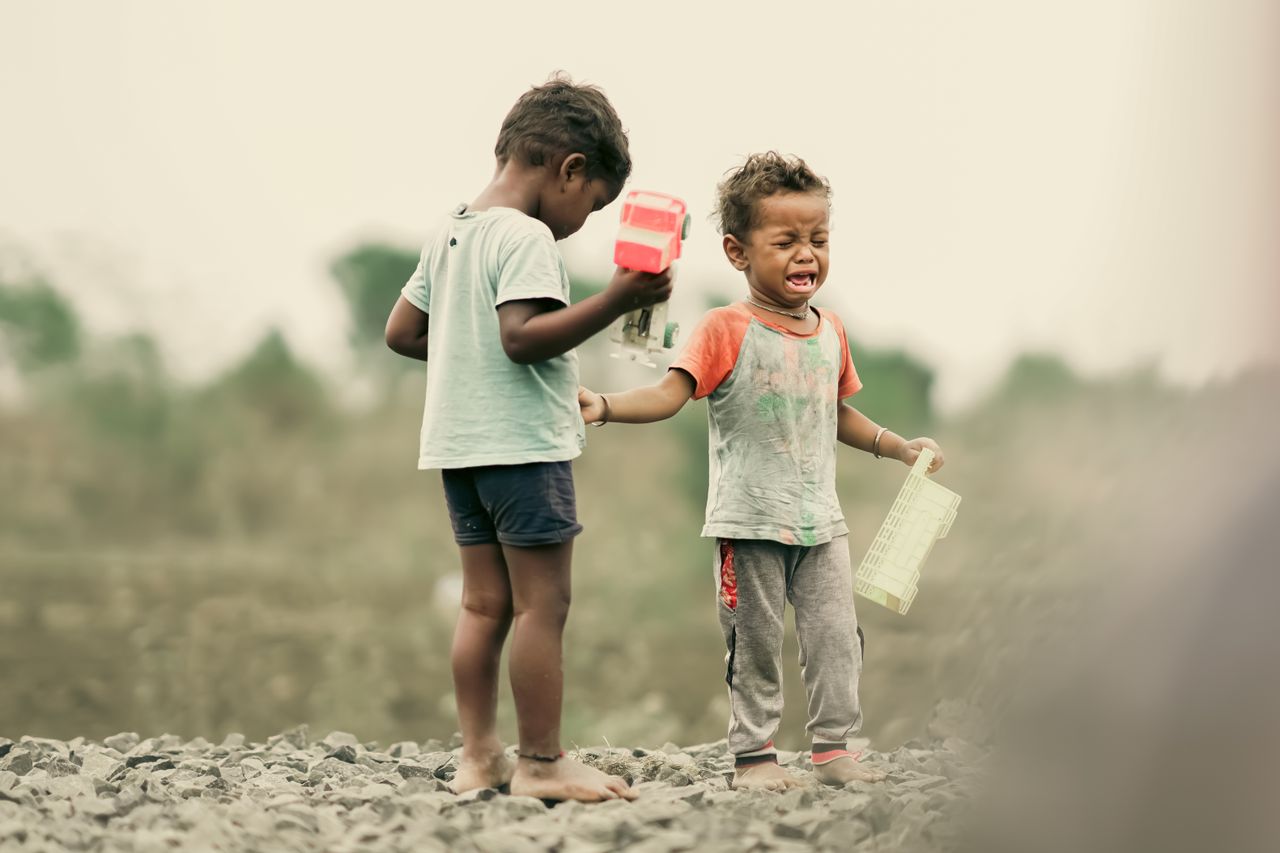 Two children play with toys in a rural field, capturing the essence of childhood emotions.