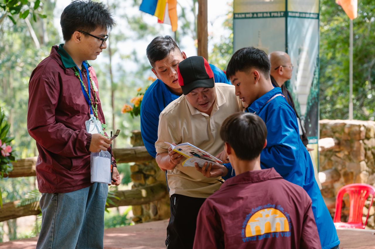 A group of adults engages in an outdoor discussion while reviewing a magazine.