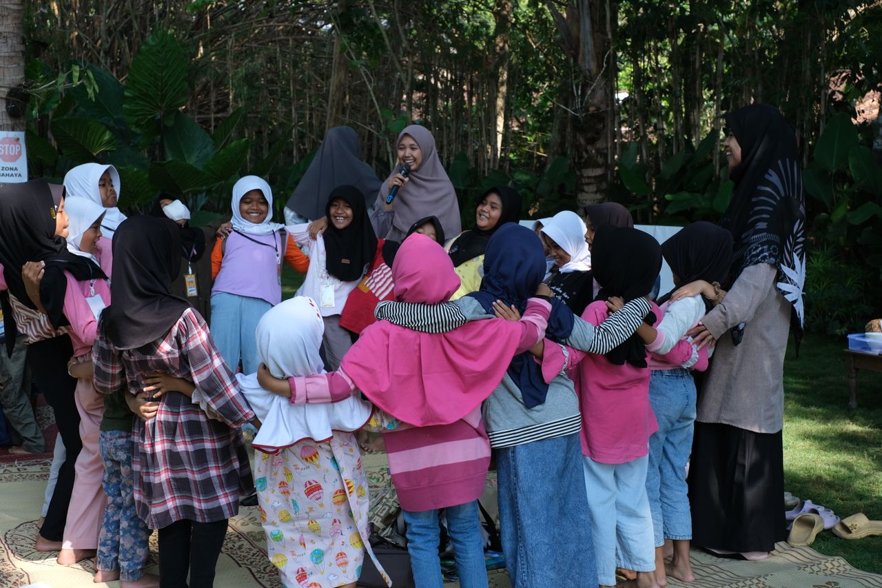 A joyful group of children participating in an outdoor activity led by adults in a lush green setting.