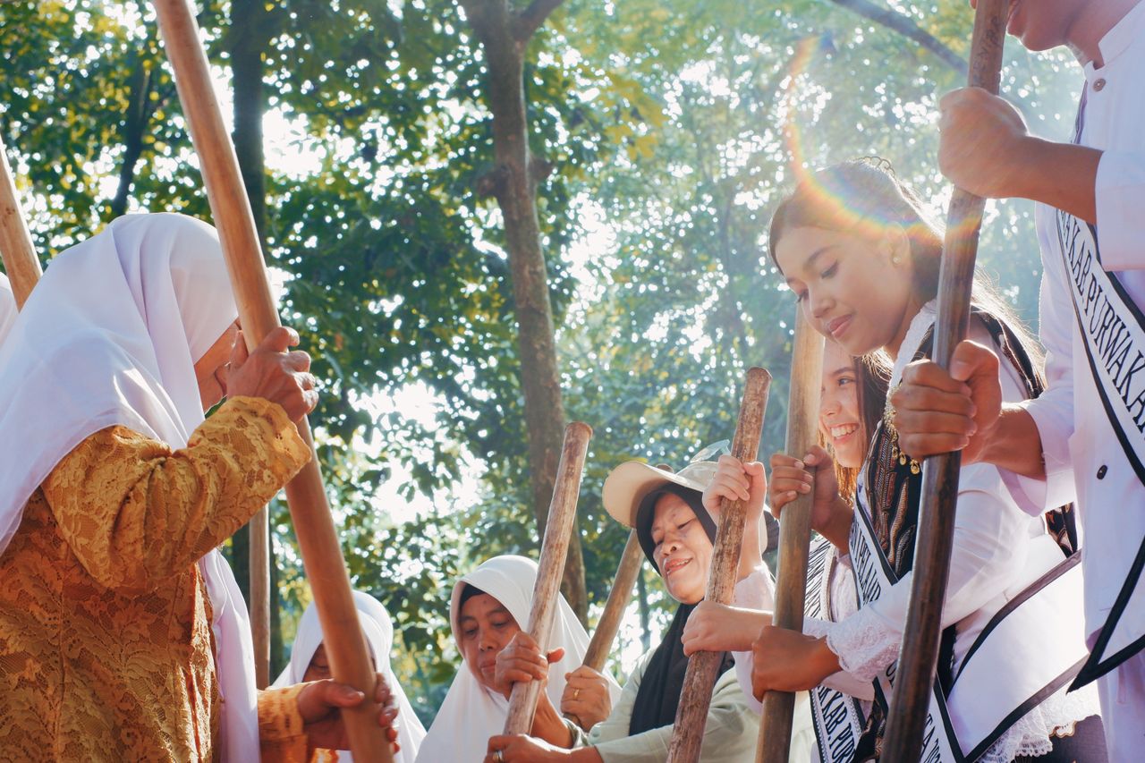 Women in traditional attire participate in a dance in West Java, Indonesia, under the sunlight.
