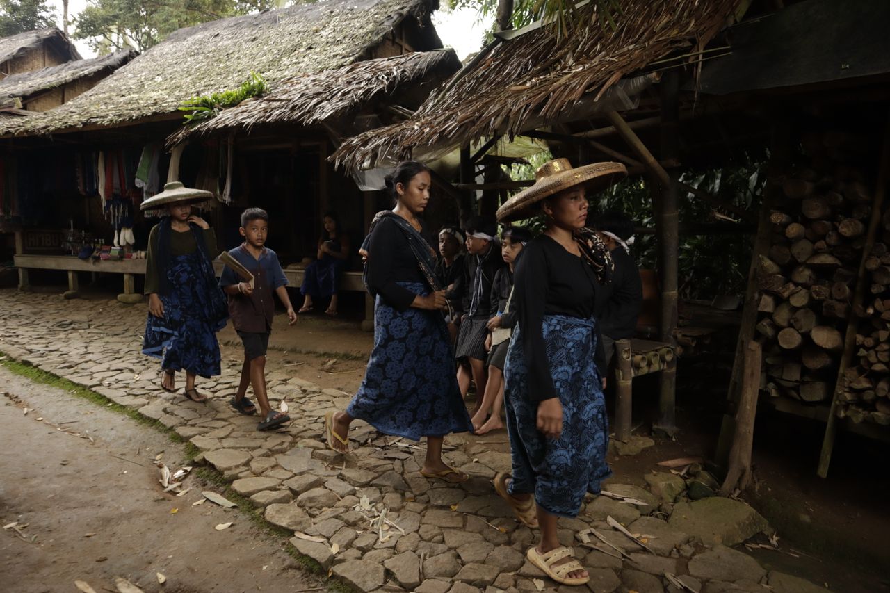 Group of people in traditional attire walking through a rustic village pathway.
